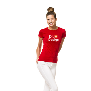 Kvinde står smilende i rød T-shirt med teksten "Dit Design", hænderne bag ryggen, iført hvide bukser. Ren hvid baggrund.