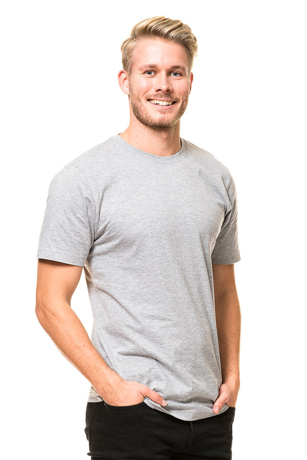 Heavy Lux T-shirt Økologisk grå En smilende mand iført en grå t-shirt står med hænderne i lommerne mod en hvid baggrund.