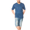 Mand iført en blå t-shirt og knælange denimshorts, står afslappet med krydsede ben og hænderne delvist i lommerne, på en hvid baggrund.