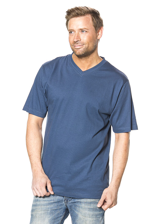 Klassisk V-hals Økologisk blue Mand iført blå T-shirt og jeans står og ser til siden med et lille smil på læben. Baggrunden er helt hvid.