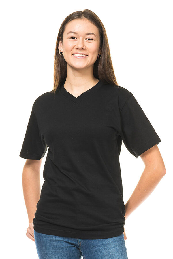 Klassisk V-hals Økologisk sort En ung kvinde iført en sort T-shirt og blå jeans smiler til kameraet. Hun står oprejst med hænderne i hoftesiden på en hvid baggrund.