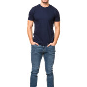 En mand står og smiler, iført en mørkeblå t-shirt, jeans og sorte sneakers, med hænderne i lommerne. Baggrunden er hvid og minimalistisk.