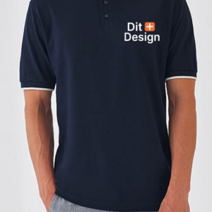 En sort poloshirt bæres af en person; teksten "Dit Design" er trykt på brystet i hvid og inkluderer et rødt plus-symbol. Baggrunden er ensfarvet lys.