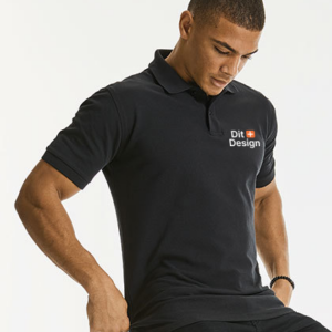 Person sidder og justerer sin sorte polo-skjorte med teksten "Dit Design" på brystet, mod en lys baggrund, mens han ser nedad.