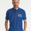 Mand står iført en blå polo-shirt med teksten "Dit Design" og et lille orange og hvidt ikon på brystet. Baggrunden er hvid.