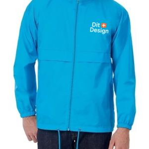 Mand iført lyseblå jakke med lynlås og snøre i bunden, står i en afslappet stilling. Tekst på jakken: "Dit Design" med en lille orange firkant. Baggrunden er neutral.