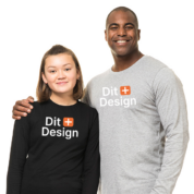 To personer står sammen, iført trøjer med teksten "Dit Design" i et studie med en hvid baggrund. Den voksne smiler og har armen om barnet.