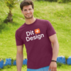 Mand iført bordeaux t-shirt med teksten "Dit Design" går i en græsklædt park. Der er en lav mur i blå og hvide farver i baggrunden.