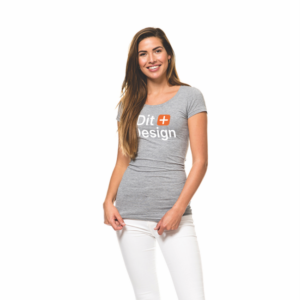 Kvinde står smilende iført grå T-shirt med teksten "Dit Design" og hvide bukser, i neutral, hvid baggrund.