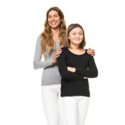 To kvinder står sammen, hvoraf den ene hviler hænderne på skuldrene af den anden; begge er iført hvide bukser og langærmede trøjer (grå og sort) på en hvid baggrund.