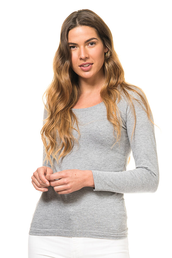 Dame Tee Langærmet grå En kvinde med langt, bølget hår står i en grå trøje og hvide bukser, kigger direkte fremad og holder sine hænder sammen. Baggrunden er hvid.