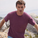 En mand iført en lilla t-shirt går op ad en stensti i et bjergrigt landskab. I baggrunden ses klipper og en fjern udsigt over havet.
