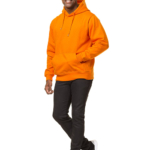 En mand i en orange hættetrøje og sorte bukser går fremad på en hvid baggrund. Han smiler, mens han bevæger sig.