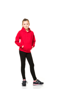 En pige iført en rød hættetrøje og sorte leggings står lidt skævt mod kameraet med hænderne i lommerne, i en hvid, minimalistisk baggrund.