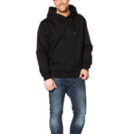 En mand iført en sort hættetrøje og blå jeans står afslappet med en hånd i lommen; baggrunden er hvid og tom.
