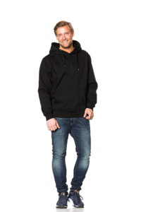 En mand iført en sort hættetrøje og blå jeans står afslappet med en hånd i lommen; baggrunden er hvid og tom.