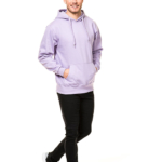 En mand i en lilla hættetrøje og sorte bukser går og smiler. Han har hænderne i lommerne og bærer sorte sneakers. Baggrunden er helt hvid.