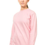 En person iført en lyserød sweatshirt står oprejst mod en hvid baggrund, ser direkte fremad og har hænderne ved siden. Personen har håret samlet i en lav hestehale og bærer øreringe.