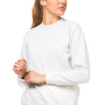 Person i hvid sweatshirt står og kigger til siden i en neutral, lys baggrund. Hun har en hestehale og hendes hænder er samlet foran hende.