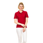 En person står og smiler iført en rød polo og hvide bukser mod en hvid baggrund.