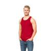 En mand iført en rød tanktop og blå jeans står med hænderne i lommerne, smilende i et hvidt baggrundsområde.