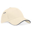 Beige kasket med buet skygge og sort kant, to ventilationshuller på hver side, ligger på en hvid overflade.