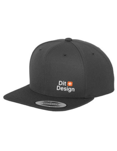 Sort kasket med flad skygge, viser teksten "Dit Design" i hvid med et orange plus. Den ligger på en hvid baggrund.