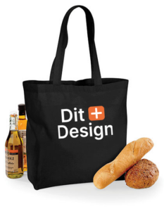 Sort mulepose med teksten "Dit Design" står oprejst. Ved siden af er der flasker med olie og brød, der skaber en indkøbs- eller picnicsammenhæng.
