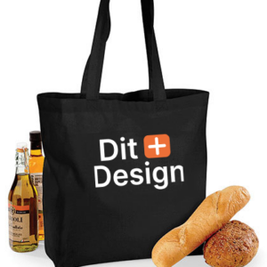 Sort mulepose med teksten "Dit Design" står oprejst. Ved siden af er der flasker med olie og brød, der skaber en indkøbs- eller picnicsammenhæng.