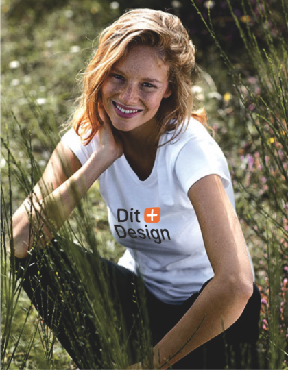 En person smiler og sidder i græsset iført en hvid T-shirt med teksten "Our Generation." Omkring hende er der vilde blomster og sollys.