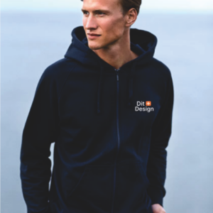 Mand iført mørk hættetrøje står ved vandkanten. Tekst på trøjen: "Dit Design." Han kigger til siden, mens det rolige vand udgør baggrunden.