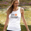 Kvinde i hvid tanktop med teksten "Dit Design," går i en græsset park med blomster i baggrunden. Hun kigger ned til siden og smiler.