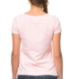 En person med en fletning iført en lyserød t-shirt og jeans står med ryggen til i et hvidt studie.