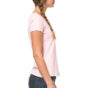 En kvinde med fletning står i profil iført en lyserød kortærmet T-shirt og mørkeblå jeans. Baggrunden er hvid.