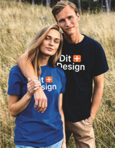 To personer iført blå og sort t-shirt med teksten "Dit Design". De står i en eng med højt græs.