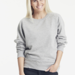 En kvinde smiler og bærer en grå trøje og sorte bukser. Tekst: "Neutral® Certified Responsibility®". Baggrunden er hvid og enkel.