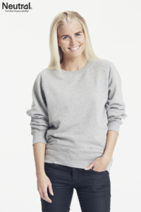 En kvinde smiler og bærer en grå trøje og sorte bukser. Tekst: "Neutral® Certified Responsibility®". Baggrunden er hvid og enkel.