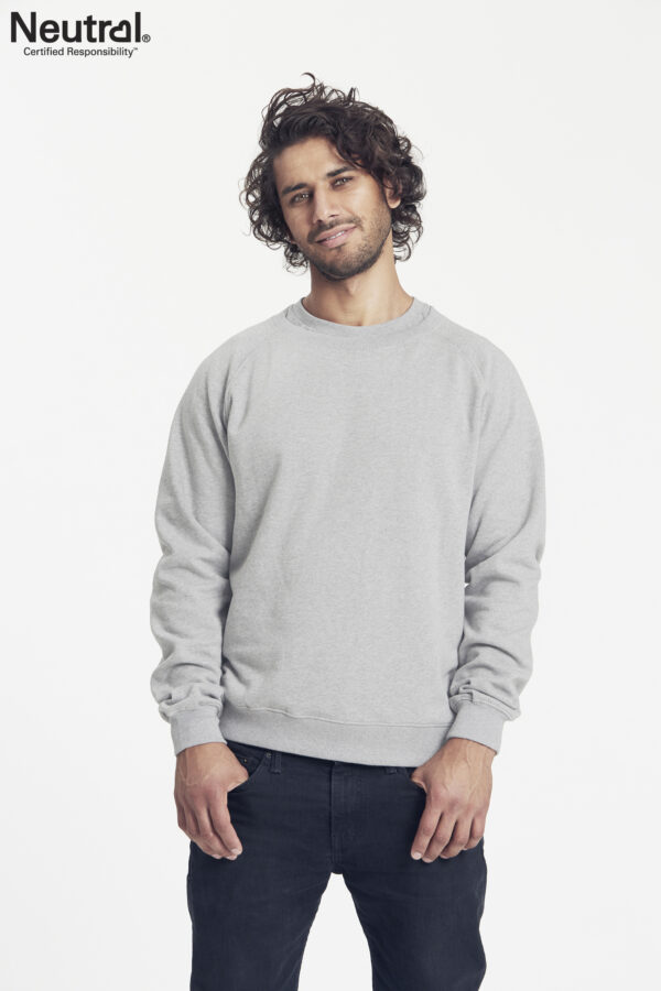O63001_M_GREY En mand iført en grå sweatshirt står afslappet med hænderne delvist i lommerne mod en hvid baggrund. Tekst: "Neutral® Certified Responsibility™".