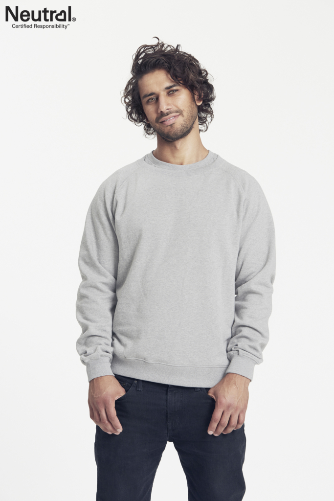 En mand iført en grå sweatshirt står afslappet med hænderne delvist i lommerne mod en hvid baggrund. Tekst: "Neutral® Certified Responsibility™".