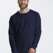 En mand med skæg og kort hår smiler, iført en mørkeblå sweatshirt og sorte bukser. I øverste venstre hjørne er teksten: "Neutral® Certified Responsibility™." Baggrunden er hvid.