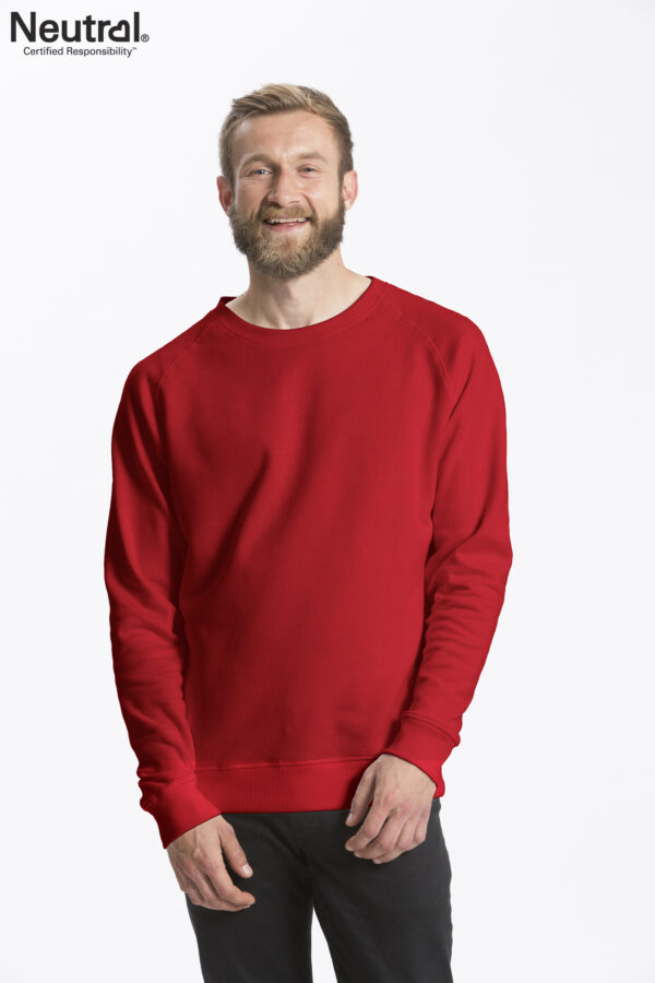 O63001_M_RED En mand iført en rød sweatshirt står smilende, med hænderne let sammenfoldet. Han har kort hår og fuldskæg. Tekst: "Neutral Certified Responsibility." Baggrunden er hvid.