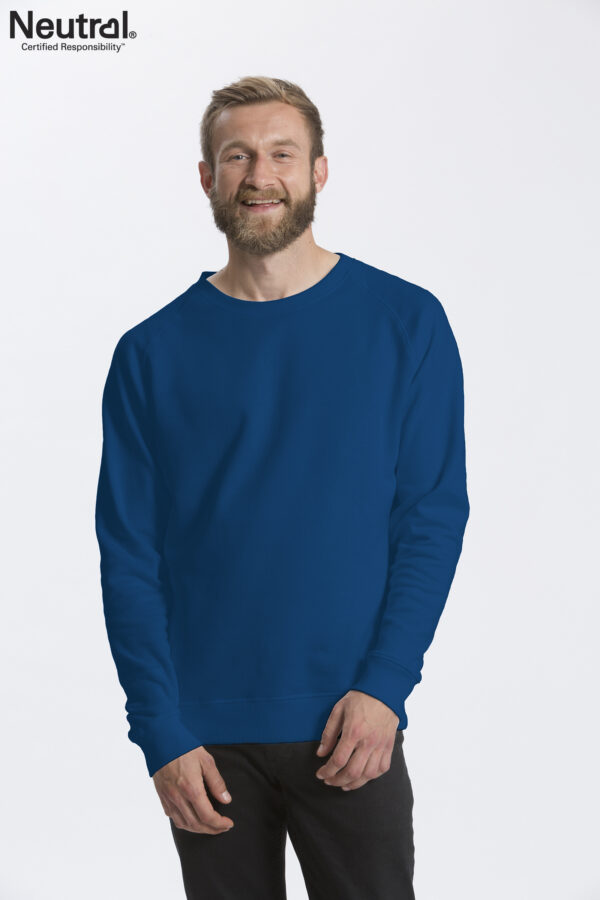 O63001_M_ROY En mand iført en blå sweatshirt smiler, mens han står foran en hvid baggrund. Tekst: "Neutral® Certified Responsibility™" i øverste venstre hjørne.