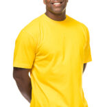 Mand iført gul t-shirt og blå jeans smiler bredt, mens han står med hænderne let gemt væk bag ryggen. Baggrunden er hvid og neutral.