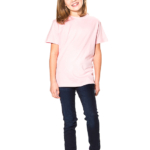 En smilende pige står oprejst, iført en lyserød T-shirt, mørkeblå jeans og lyserøde sko. Baggrunden er helt hvid og minimalistisk.