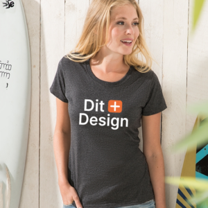 Kvinde står og smiler iført en sort T-shirt med teksten "Dit Design." Hun befinder sig i et lyst rum ved en surfbræt med skrift.