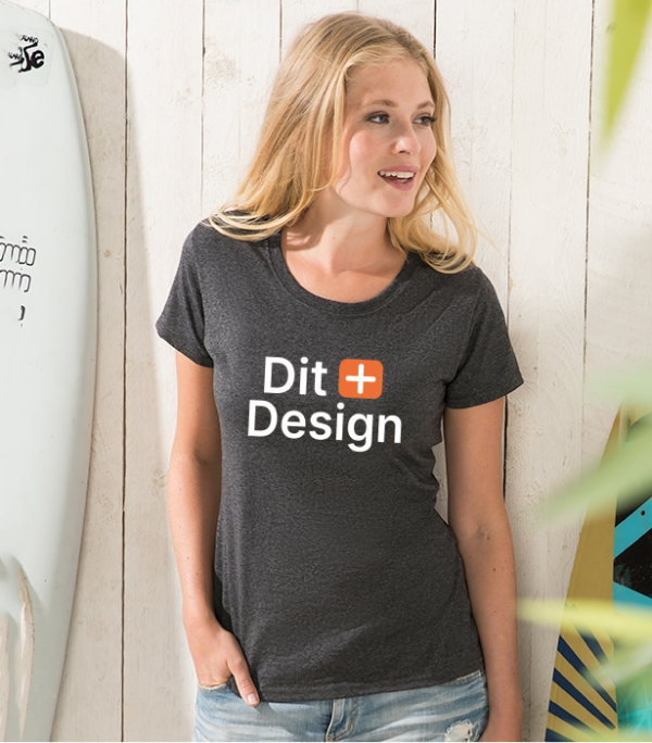 Kvinde står og smiler iført en sort T-shirt med teksten "Dit Design." Hun befinder sig i et lyst rum ved en surfbræt med skrift.