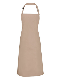 Beige forklæde hænger lige ned fra halsstroppen. Enkel og elegant udformning uden lommer. Baggrunden er ensfarvet hvid, fremhævende forklædets rene linjer og minimalistiske design.