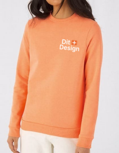 Trøje i orange bæres af en person, tekst "Dit Design" på trøjen. Personen står i et neutralt, lyst rum, iført lyse bukser.