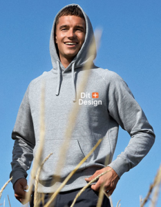 Mand iført grå hættetrøje står smilende. Tekst på trøjen: "Dit Design." Blå himmel og tørre kornstilke i baggrunden.