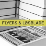 Bunker af printede materialer, hvor en bunke viser flyers og løse blade med teksten "FLYERS & LØSBLADE". Kontexten er en kontorlignende lagerplads.
